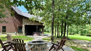 A rustic lodge with a stone fireplace and two Adirondack chairs in a stone fire pit area. - Gated Hilltop Luxury Lodge on 100 acres - Relax and Enjoy AMAZING VIEWS (Smithville)