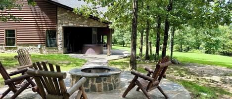 Un chalet rustique doté d’une cheminée en pierre et de deux fauteuils Adirondack disposés autour d’un foyer en pierre.