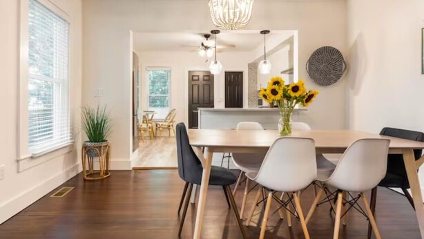 A modern dining area with a wooden table, white chairs, and a chandelier. - Northfork Townhouse walk to all (Greenport)