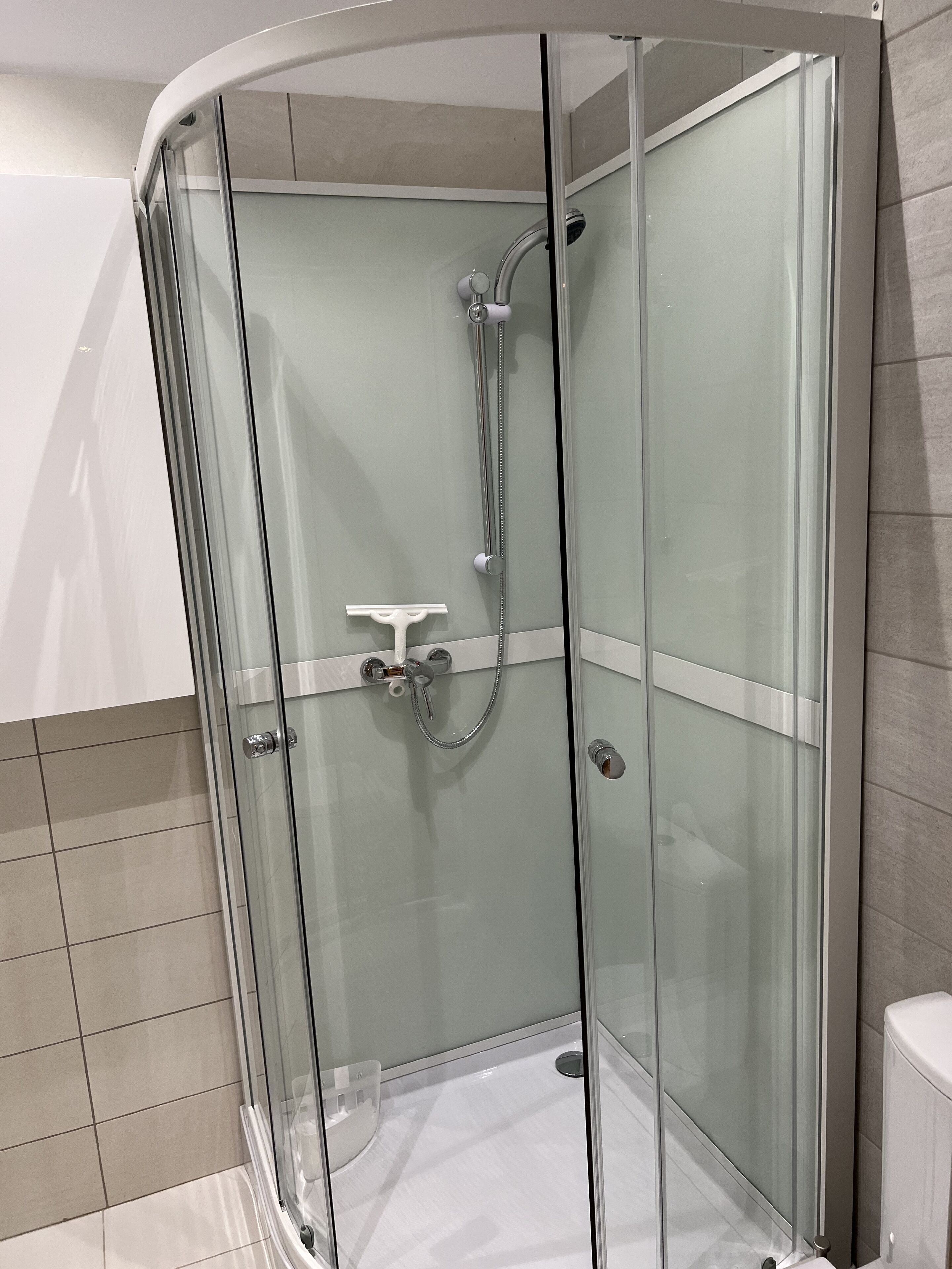 Cabina de ducha con paredes de vidrio, ducha de mano y grifo empotrado.