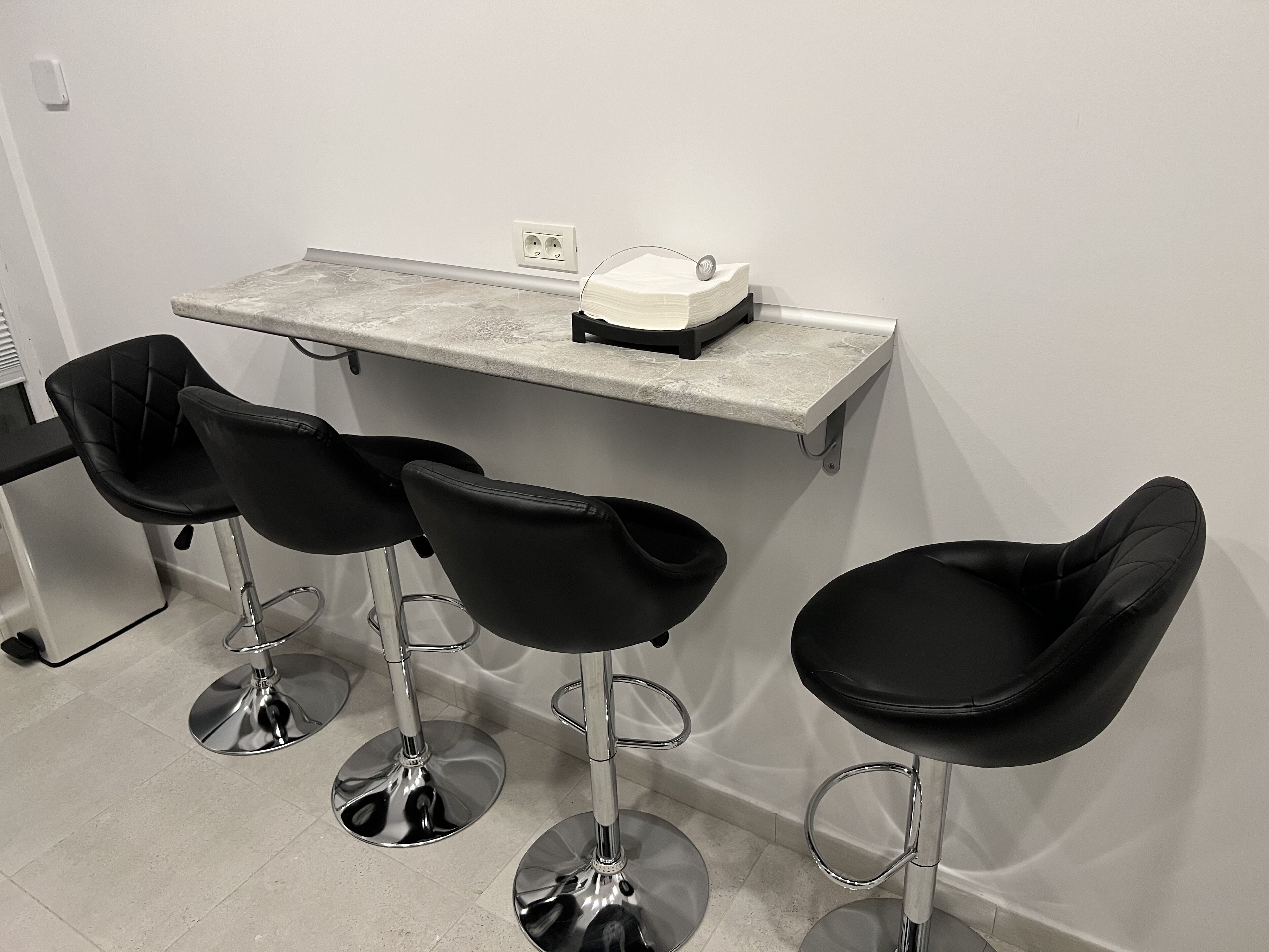 A bar area with three black bar stools and a countertop with a coffee machine.