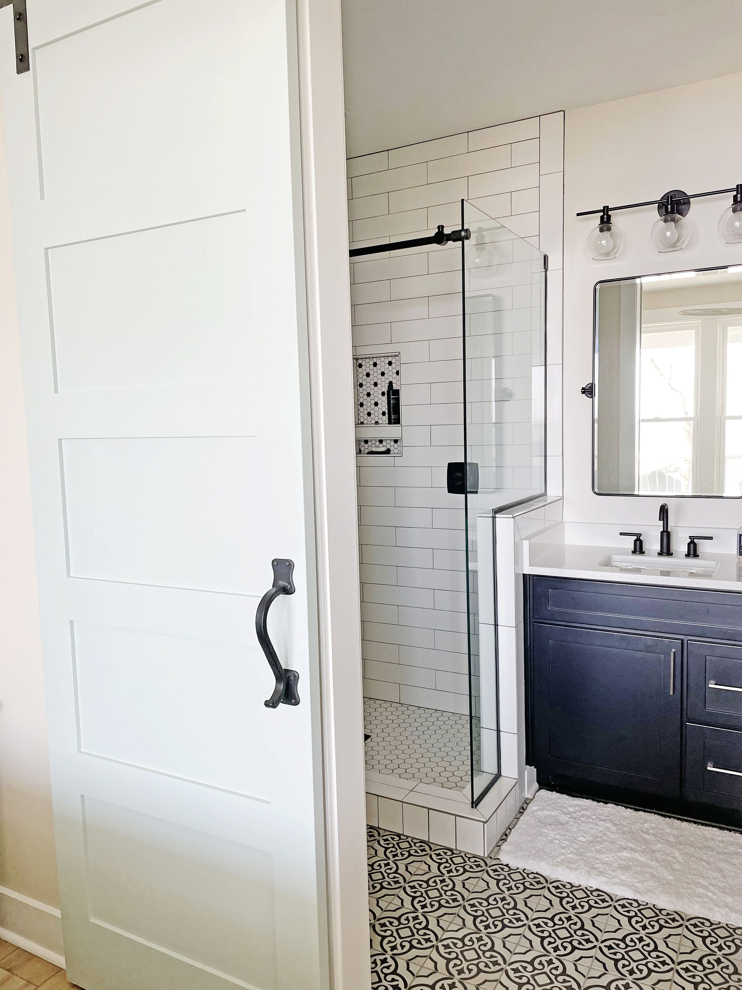 A modern bathroom with a glass shower enclosure, white tiled walls, a dark blue vanity, and a large mirror.