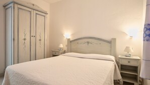 A bedroom with a bed, two bedside tables, a wardrobe, and wall-mounted lamps. - Appartamenti Porto Coda Cavallo (San Teodoro)