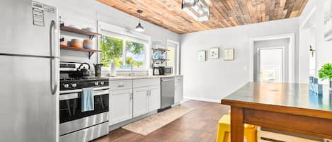 A modern kitchen with stainless steel appliances, wooden flooring, and a wooden ceiling.