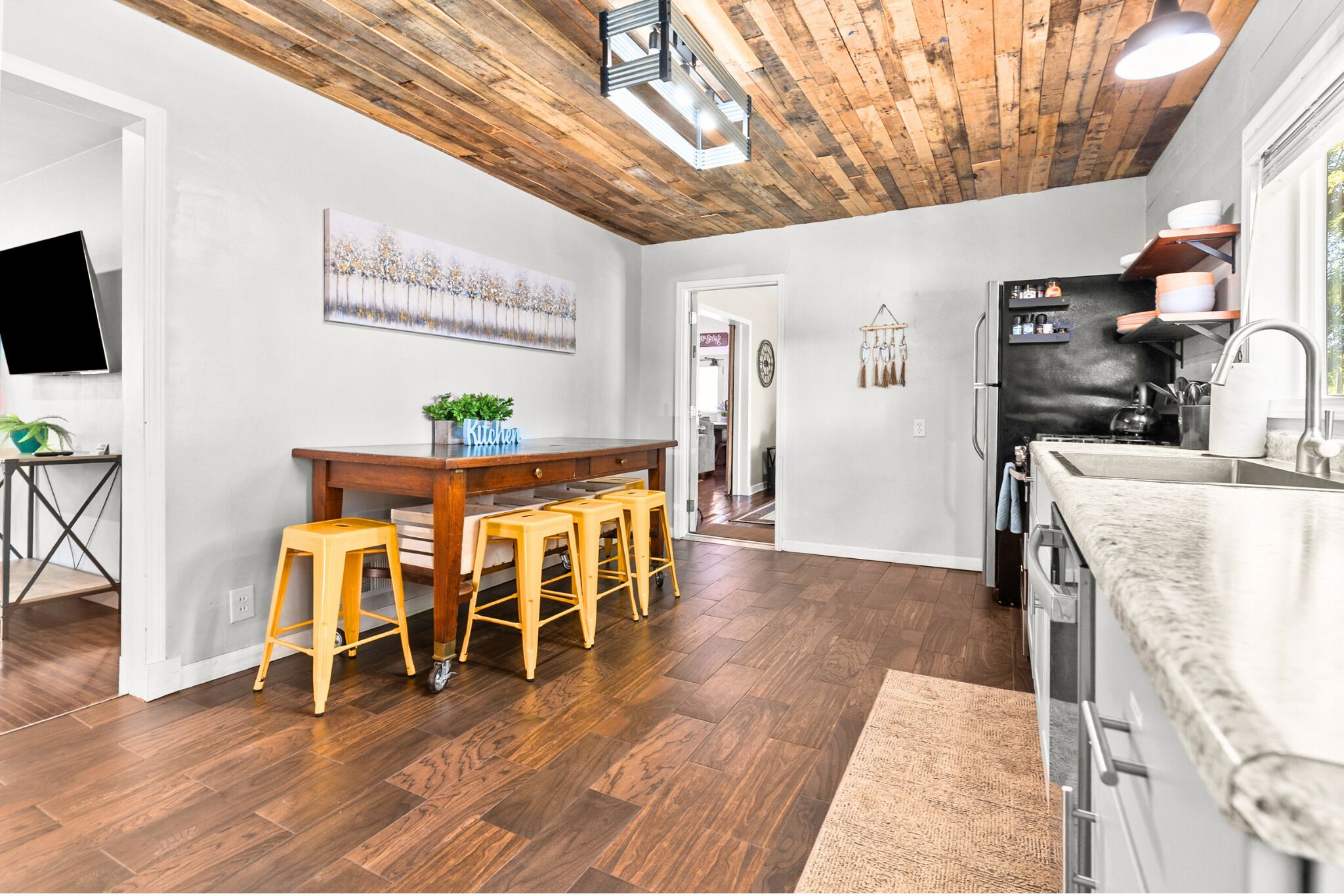 A modern kitchen with wooden flooring, a bar area with stools, and a built-in refrigerator.