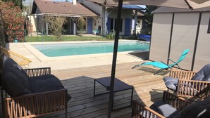 An outdoor deck with wooden furniture, a pool, and a covered area with a pergola. - Bigazen - Family house sleeps 8 (Biganos)