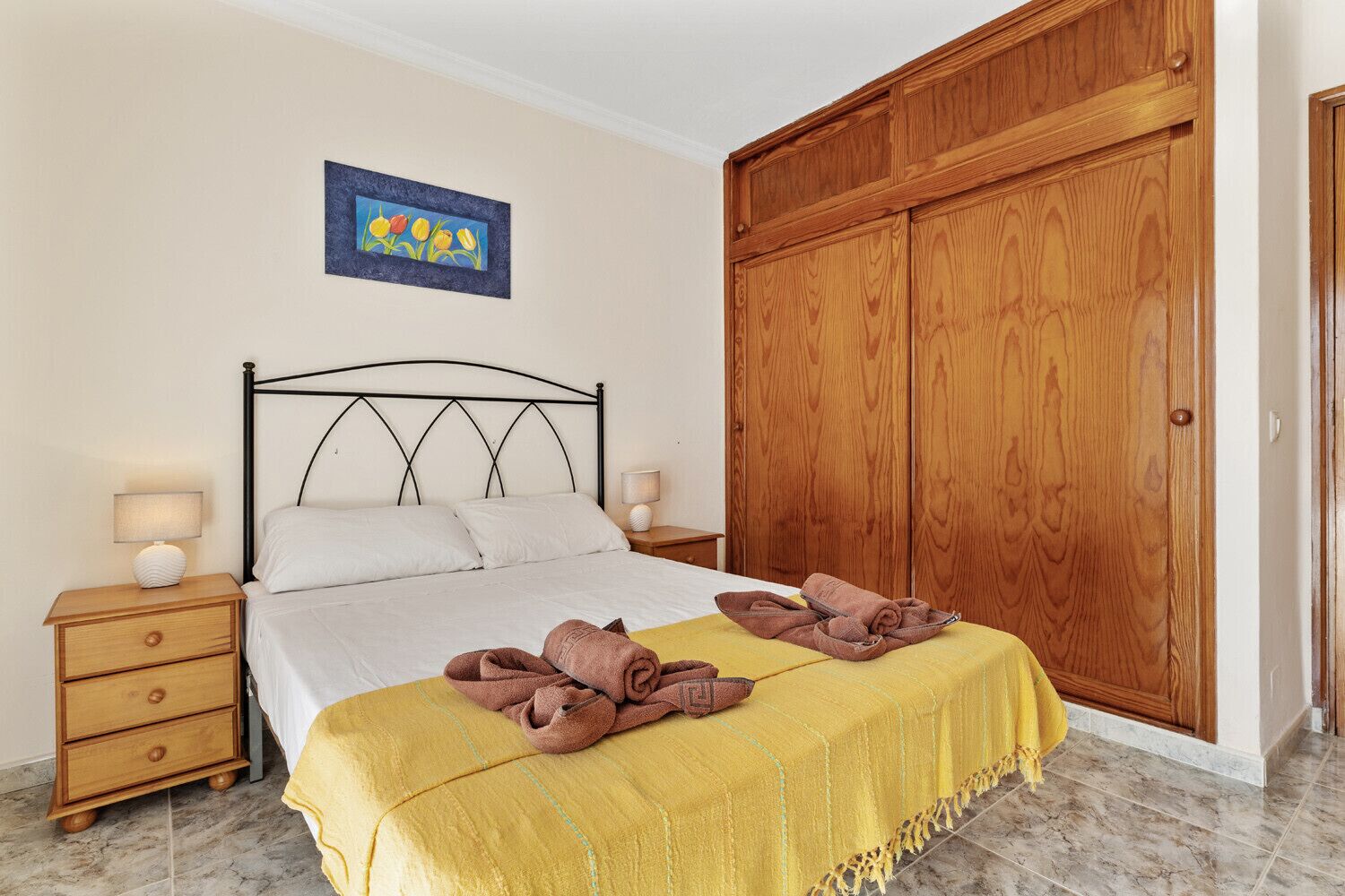 A bedroom with a bed, wooden wardrobe, nightstands, and a painting on the wall.