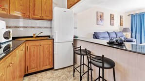 Eine kompakte Küche mit Holzausbau, einem weißen Kühlschrank, einer Mikrowelle und einer kleinen Bar mit Sitzgelegenheiten.