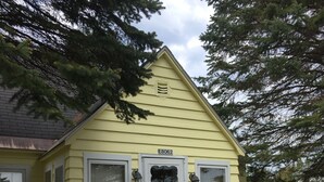 Une maison jaune avec une porte et des fenêtres blanches, une terrasse rouge et une boîte aux lettres portant le numéro E8062.