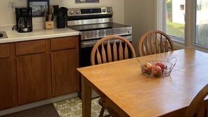 Une cuisine avec des meubles de rangement en bois, une cuisinière, une machine à café et une table à manger avec des chaises.
