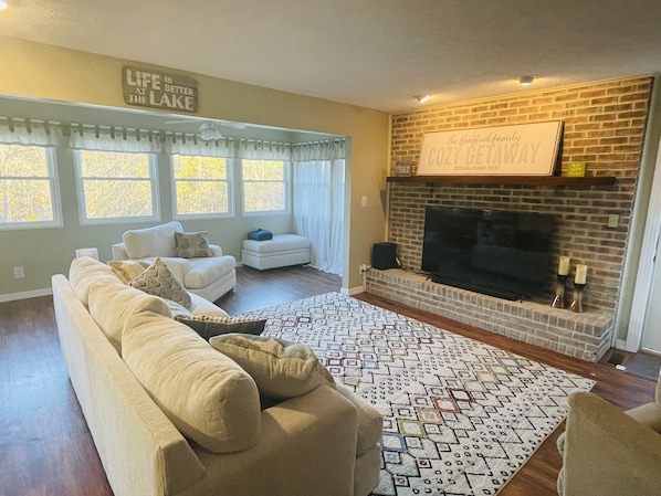 Una sala de estar con un sofá color beige, un tapete estampado, una chimenea y un letrero sobre la chimenea.