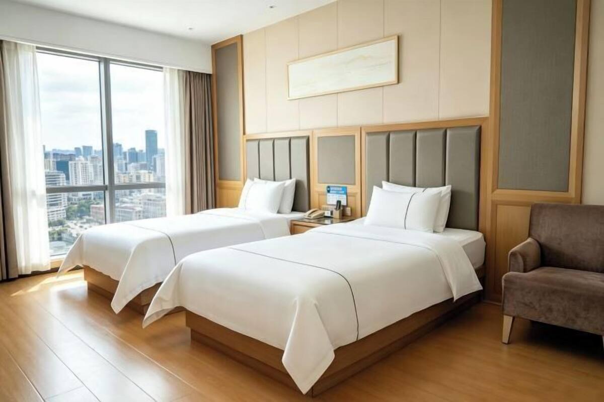 A hotel room with two beds, a city view, a large window, and a framed picture on the wall.