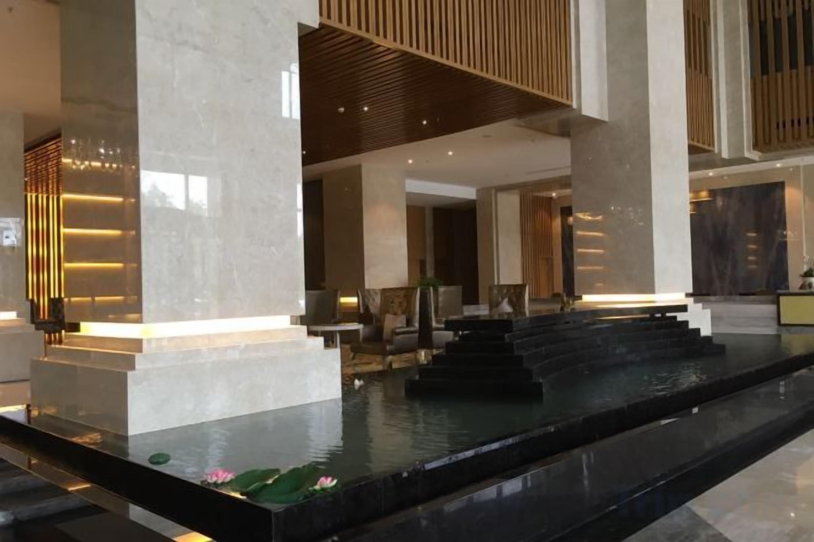 A modern lobby with a marble reception desk, a water feature with steps, and a seating area.
