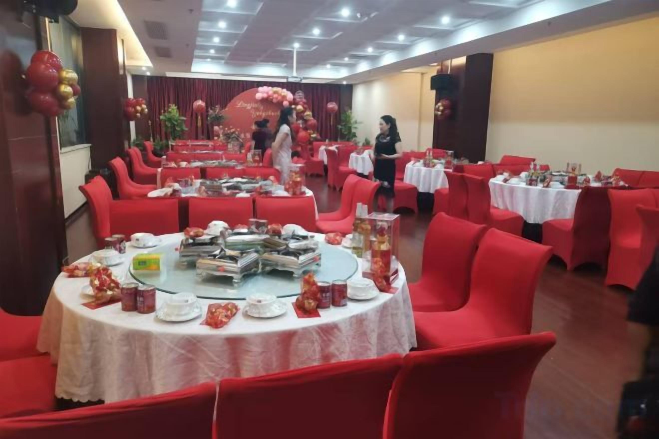 A banquet hall with round tables, red chairs, and a central floral arrangement.
