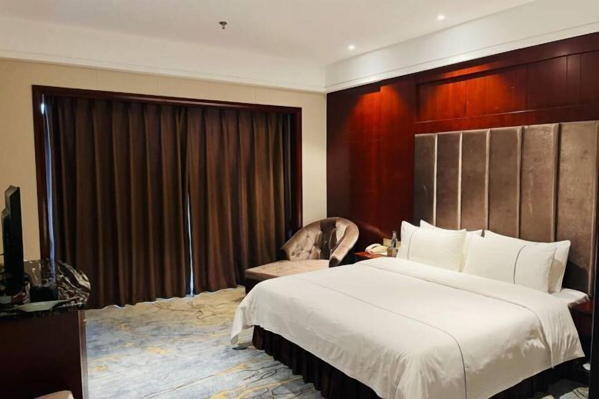 A hotel room with a large bed, a desk with a chair, a television, and a window with curtains.