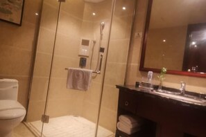 Une salle de bain moderne dotée d’une douche à parois de verre, d’un meuble-lavabo avec un plan de travail foncé et d’un grand miroir au-dessus du lavabo.