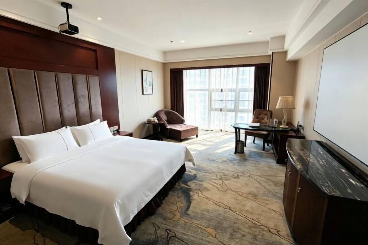 A hotel room with a large bed, a desk, a chair, and a television.