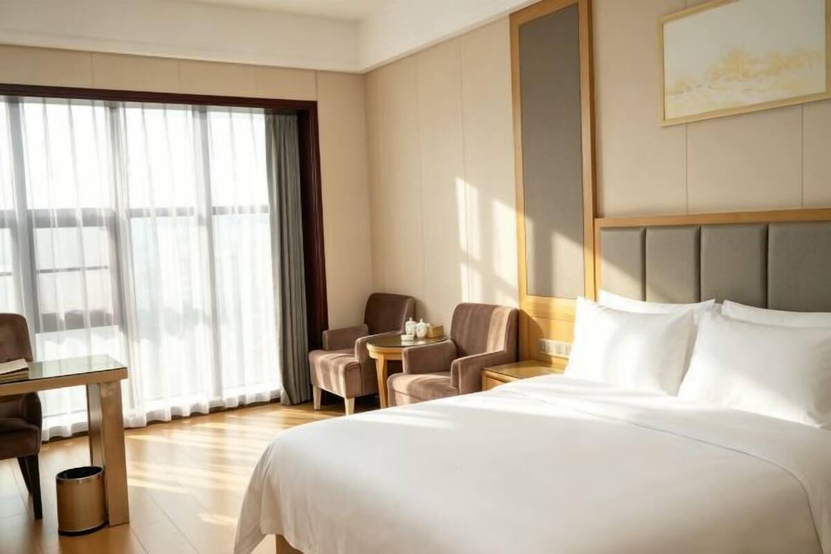 A hotel room with a bed, a desk, a chair, a small table, and a window with curtains.