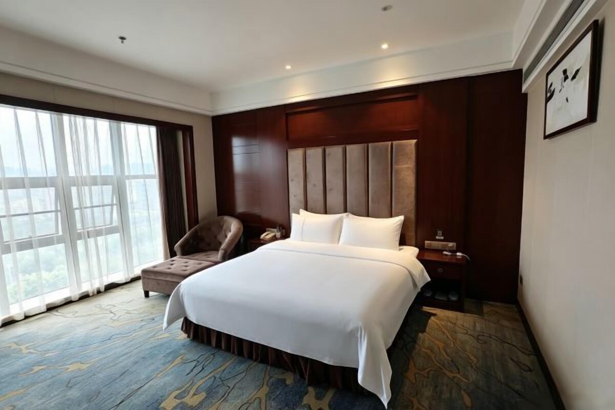 A hotel room with a large bed, a chair, a nightstand, and a window with curtains.