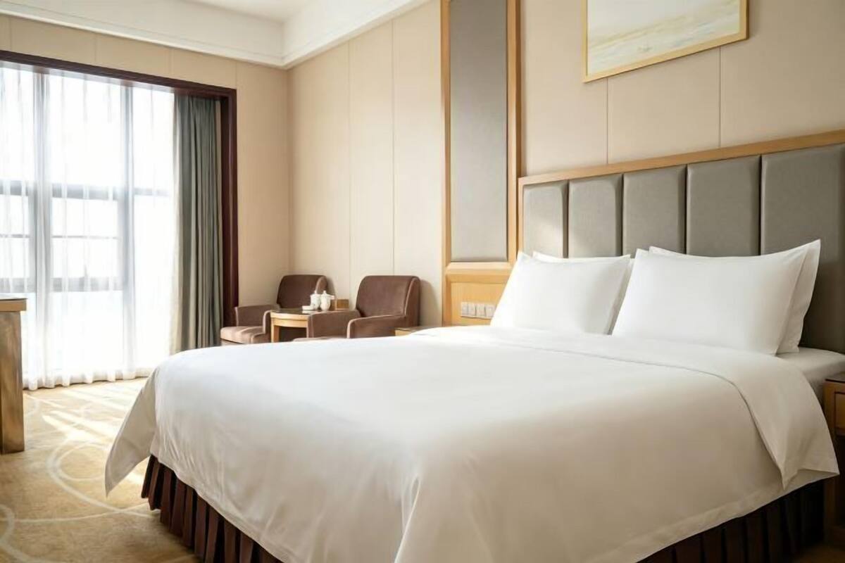 A hotel room with a large bed, a desk, a chair, and a view of the outdoors.