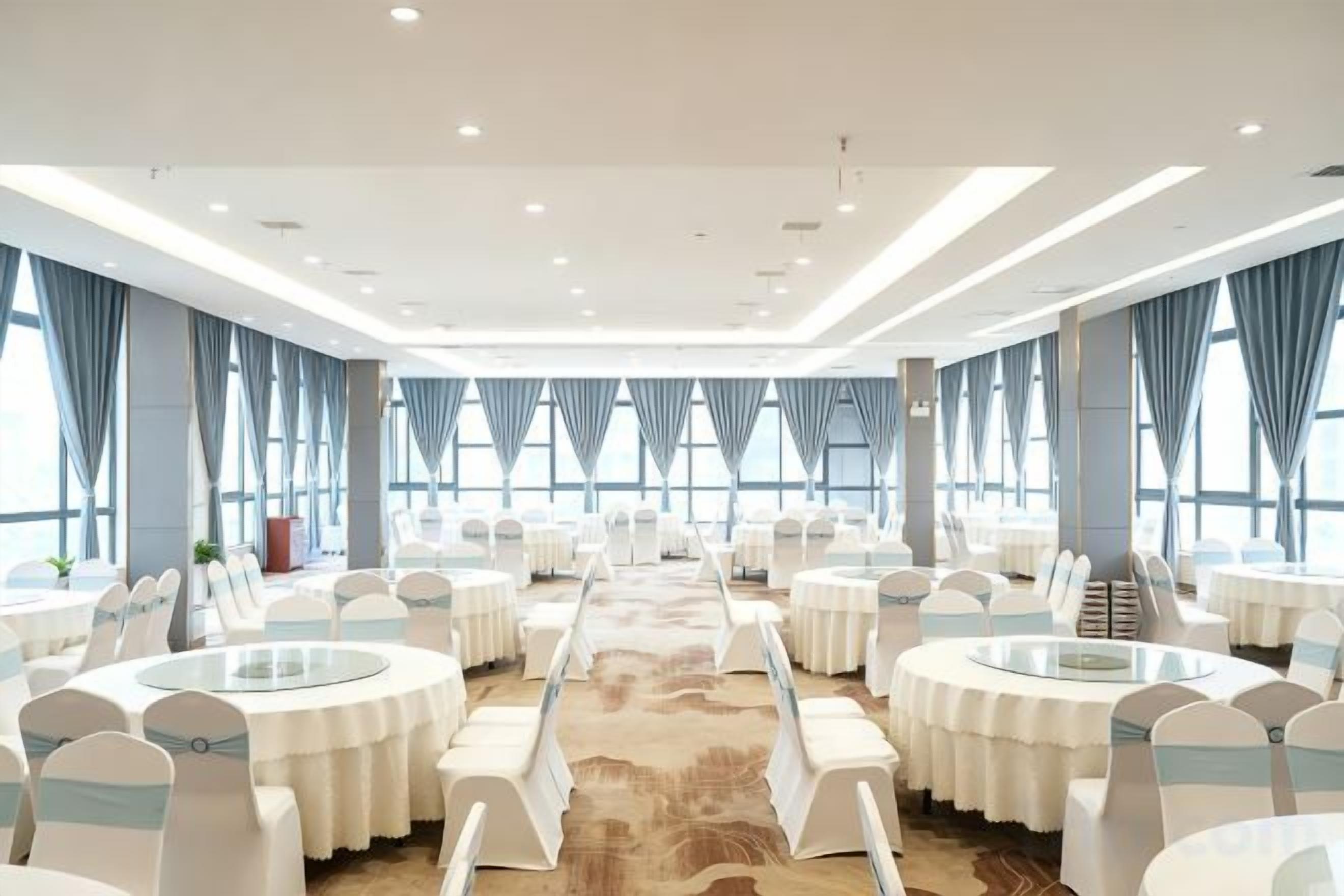 Un salón de conferencias con mesas y sillas redondas, ventanas amplias y suelo alfombrado.