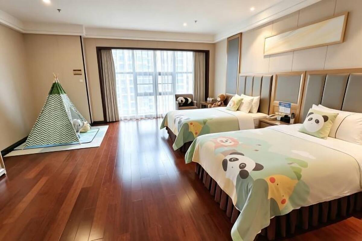 A hotel room with two beds, a window with curtains, a small table, and a green and white tent.