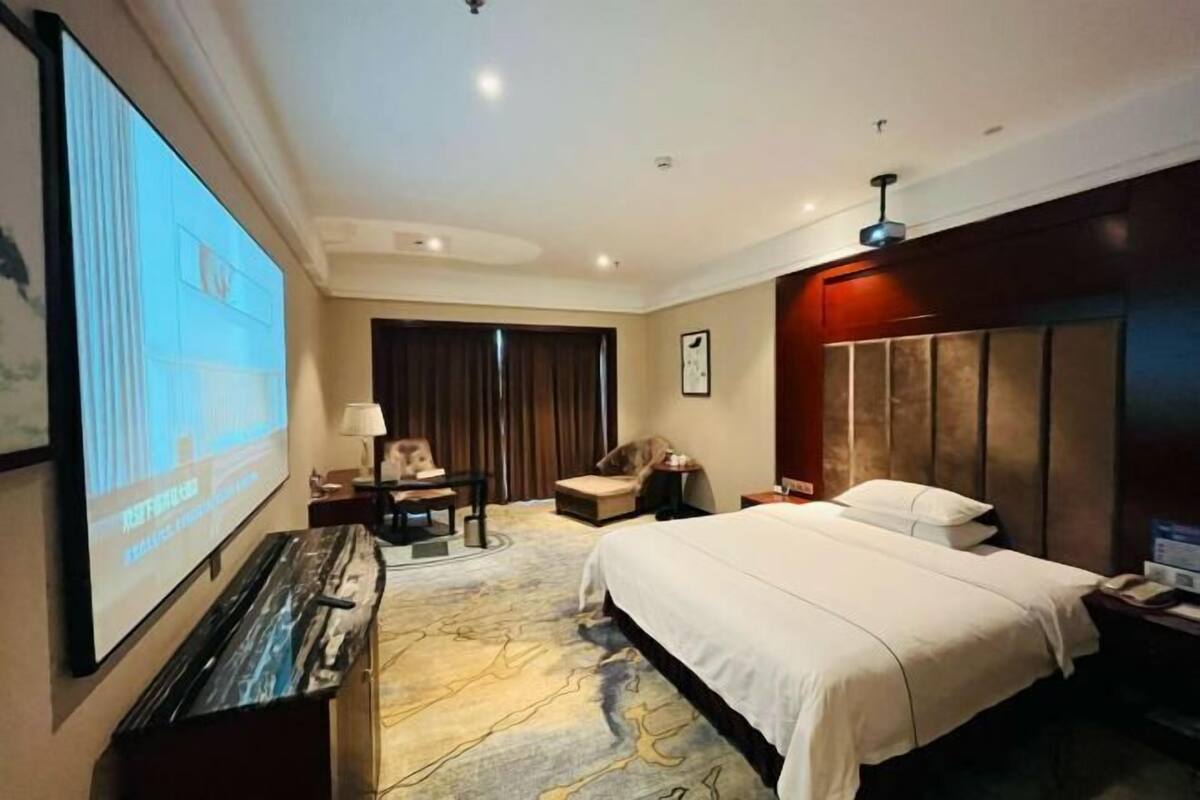 A hotel room with a bed, a desk, a chair, a television, and a large window.