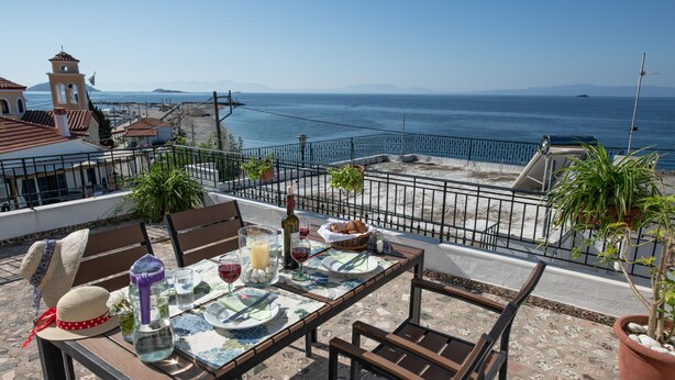 Una terraza con mesa lista para comer, con vistas al mar y cielo despejado.
