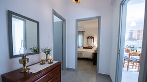 Un pasillo con un aparador de madera, un espejo y una vela encendida. Se ve una puerta que da a un dormitorio con cama y espejo.