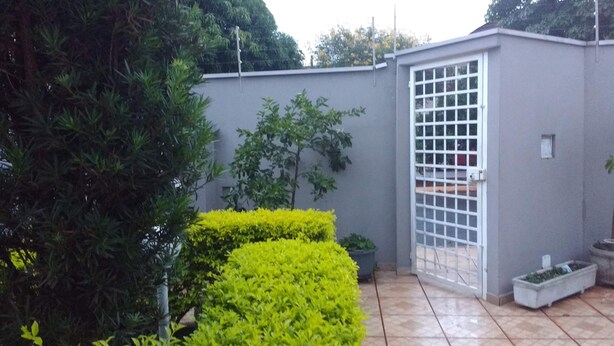 A gated courtyard with a tiled floor, a small hedge, and a tall tree.