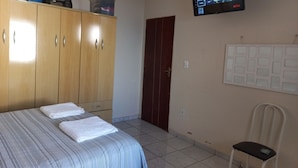 A hotel room with a bed, a wardrobe, a television mounted on the wall, a chair, and a door.