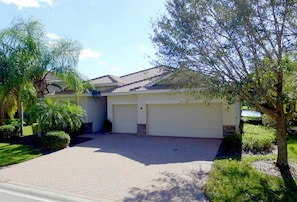 A residential house with a paved driveway, two garage doors, and well-maintained landscaping including trees and bushes. - TOP FLORIDA'S Villa Lazy River (North Fort Myers)