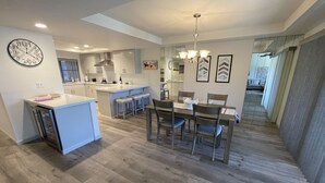 Une cuisine moderne dotée d’un îlot central, d’un coin repas avec des chaises en bois et d’une grande fenêtre qui laisse entrer la lumière naturelle.