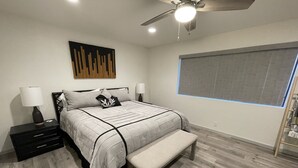 Une chambre à coucher comprenant un lit, des tables de chevet, un banc, un ventilateur de plafond et une fenêtre.