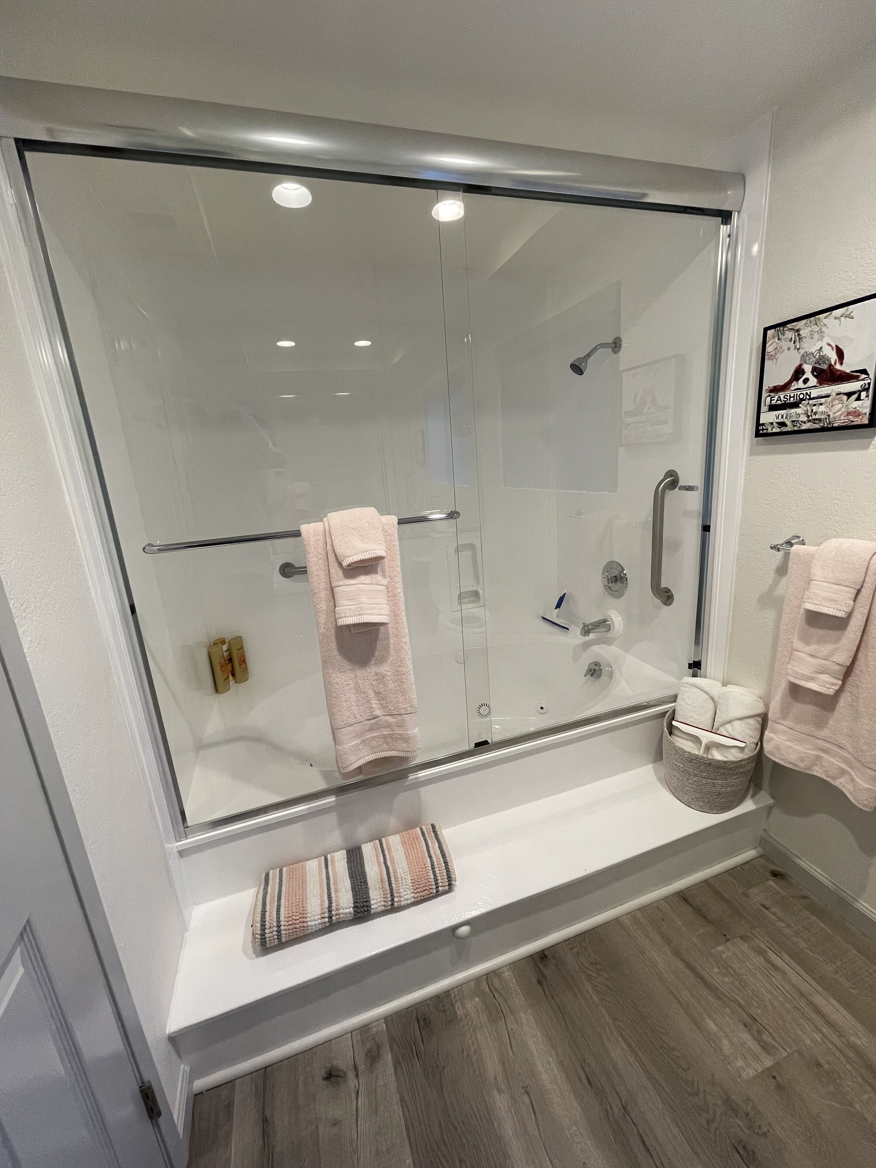 A modern bathroom with a glass-enclosed shower, white fixtures, and a wooden floor.