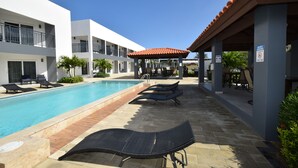 Un espace piscine avec des chaises longues, un coin salon abrité et un panneau indiquant les heures de silence.