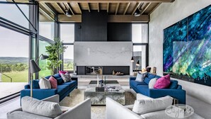 A modern living room with a fireplace, blue sofas, and a large abstract painting. - 5bdrm 7bath modern oasis in Creemore! Pool! Hot Tub! Sauna! Podcast Media Rm! (Creemore)