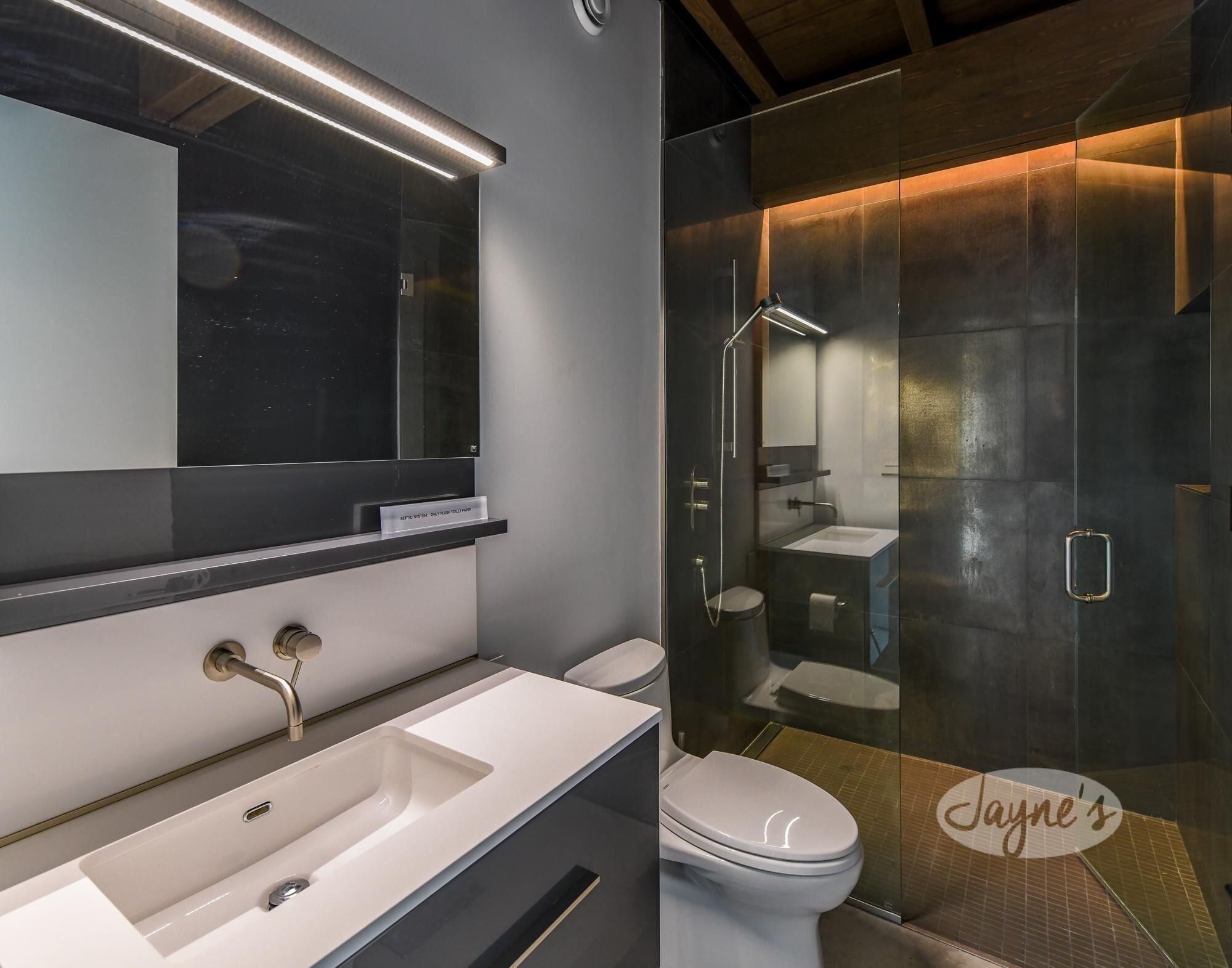 A modern bathroom with a large mirror, a white sink, and a glass-enclosed shower area.