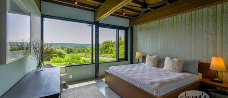 Un dormitorio con una cama grande, un escritorio y vistas al verdor.