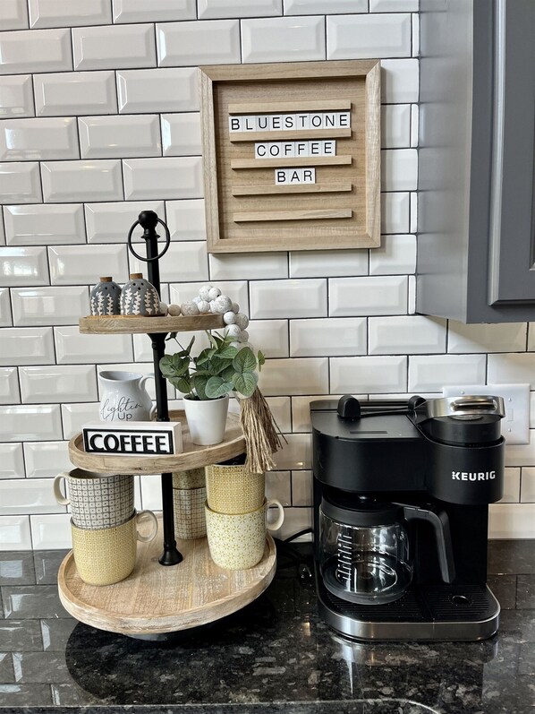 En kaffestation med kaffemaskine, en bakke med kopper og et skilt der siger 'BLUESTONE COFFEE BAR'.