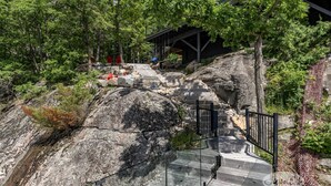 A staircase leading up a rocky path surrounded by trees, with a covered structure in the background. - SW Exposure at this 4 bdrm, 3 bath cottage with stunning views of Lake Muskoka! (Gravenhurst)
