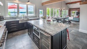 A modern kitchen with a large island, dark cabinetry, and a view of the outdoors. - SW Exposure at this 4 bdrm, 3 bath cottage with stunning views of Lake Muskoka! (Gravenhurst)