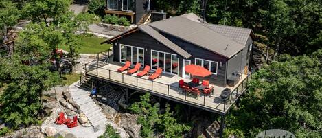 A modern cabin with a deck, outdoor seating, and a staircase leading to a second floor.