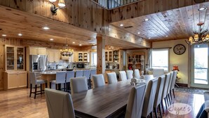 A spacious kitchen with wooden cabinets, a large island, and a dining area with a long table and chairs. - Unique 8 bed 5bath cottage on the Joe River! (Port Carling)