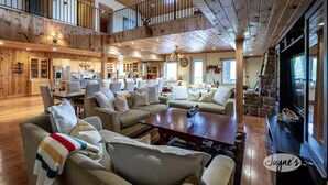 A spacious living area with multiple seating options, a kitchen in the background, and a stone fireplace. - Unique 8 bed 5bath cottage on the Joe River! (Port Carling)