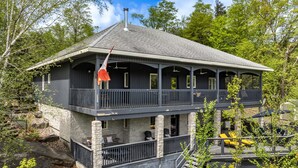 A two-story house with a balcony, stone foundation, and a chimney. - Unique 8 bed 5bath cottage on the Joe River! (Port Carling)