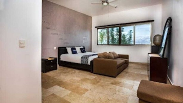 A bedroom with a bed, a sofa, a window, and a ceiling fan.