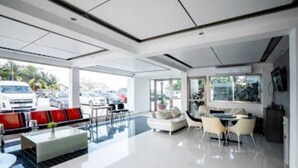 A modern hotel lobby with a spacious seating area, a dining table, and a large window offering a view of parked cars outside.