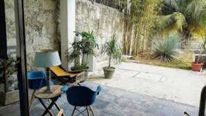 An outdoor seating area with a stone wall, a blue chair, a wooden chair, and a lamp.