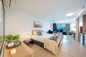 Ein modernes Hotelzimmer mit Bett, Nachttisch, Lampe und Blick auf den Balkon.